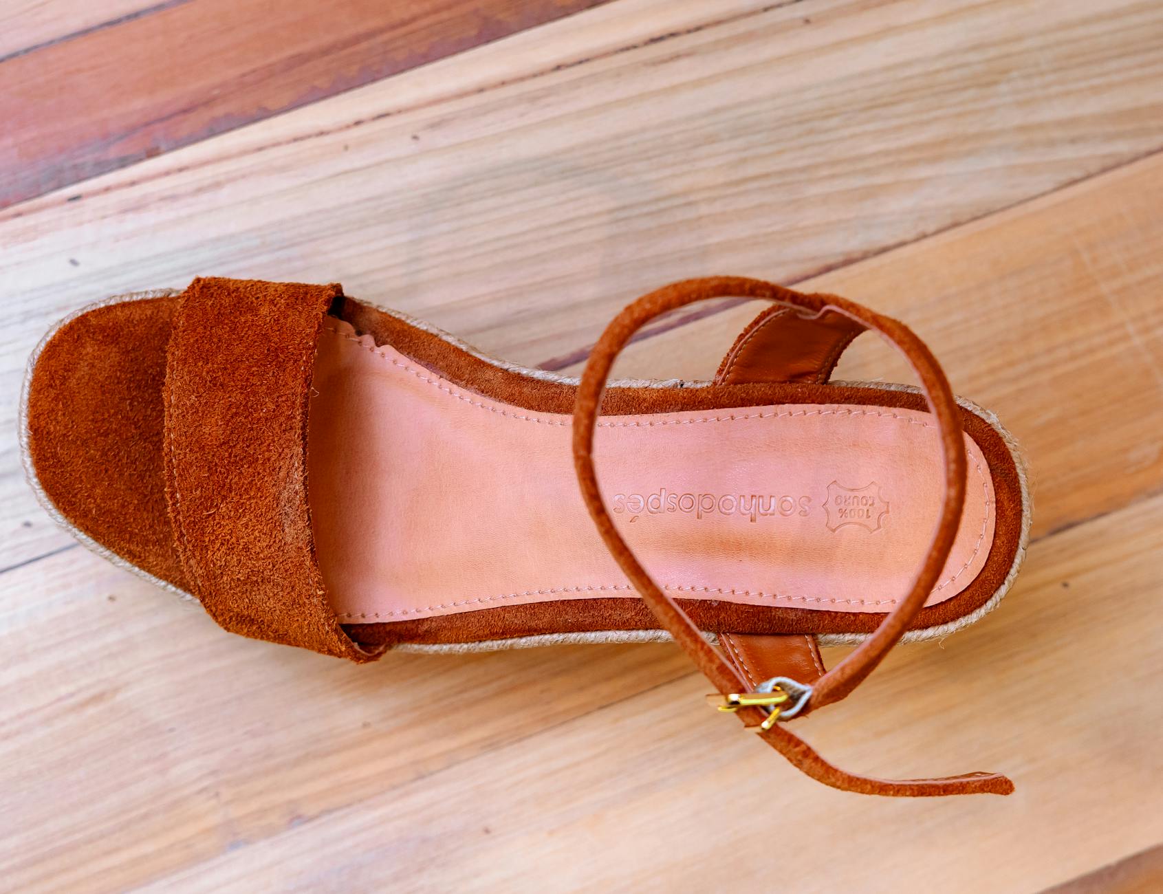 Brązowy zamszowy sandał z paskiem na kostce na drewnianej podłodze