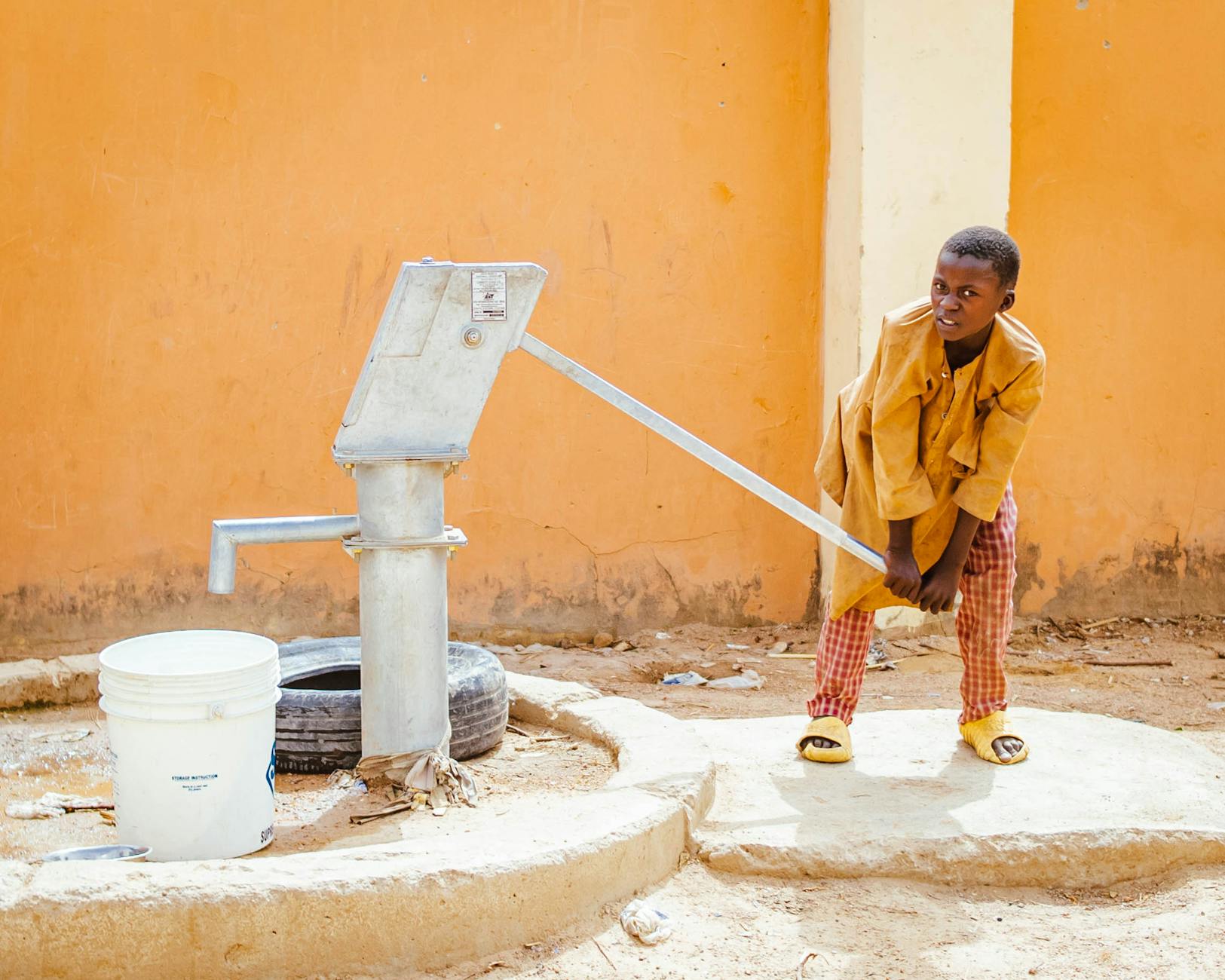Dziecko pompujące wodę ręczną pompą w afrykańskiej wiosce