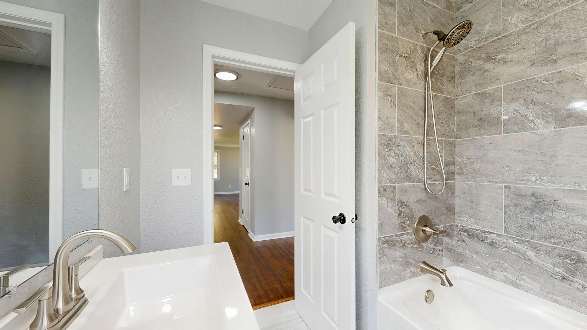 Nowoczesna łazienka w szarych płytkach z otwartymi drzwiami i armaturą