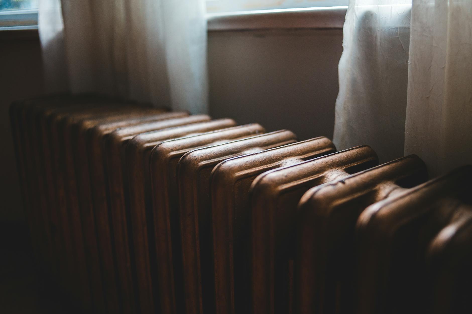 Stary żeliwny grzejnik pod oknem z firanką w mieszkaniu