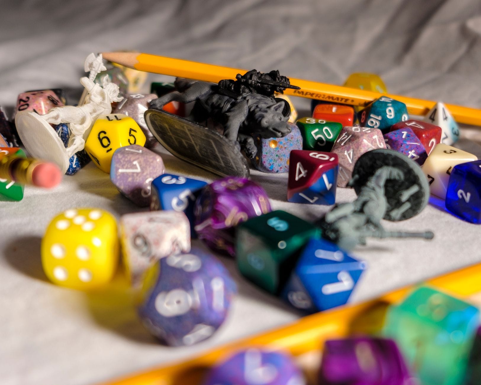 Wielokolorowe kości do RPG, ołówki i figurki zwierząt na stole