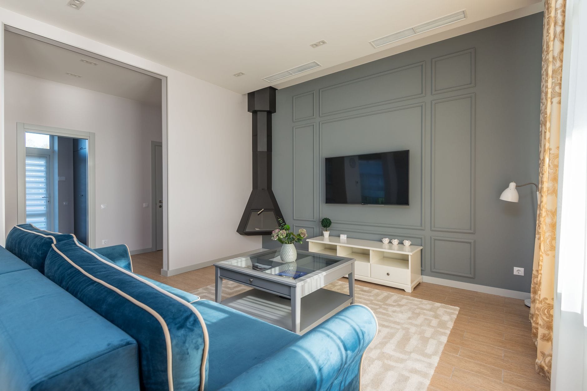 Salon z niebieską sofą i telewizorem na ścianie z eleganckim wykończeniem