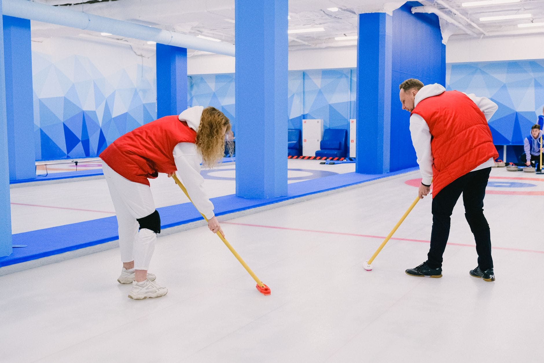 Mężczyzna i kobieta trenują curling, zamiatając lód na tafli lodowiska Mężczyzna i kobieta trenują curling, zamiatając lód na tafli lodowiska