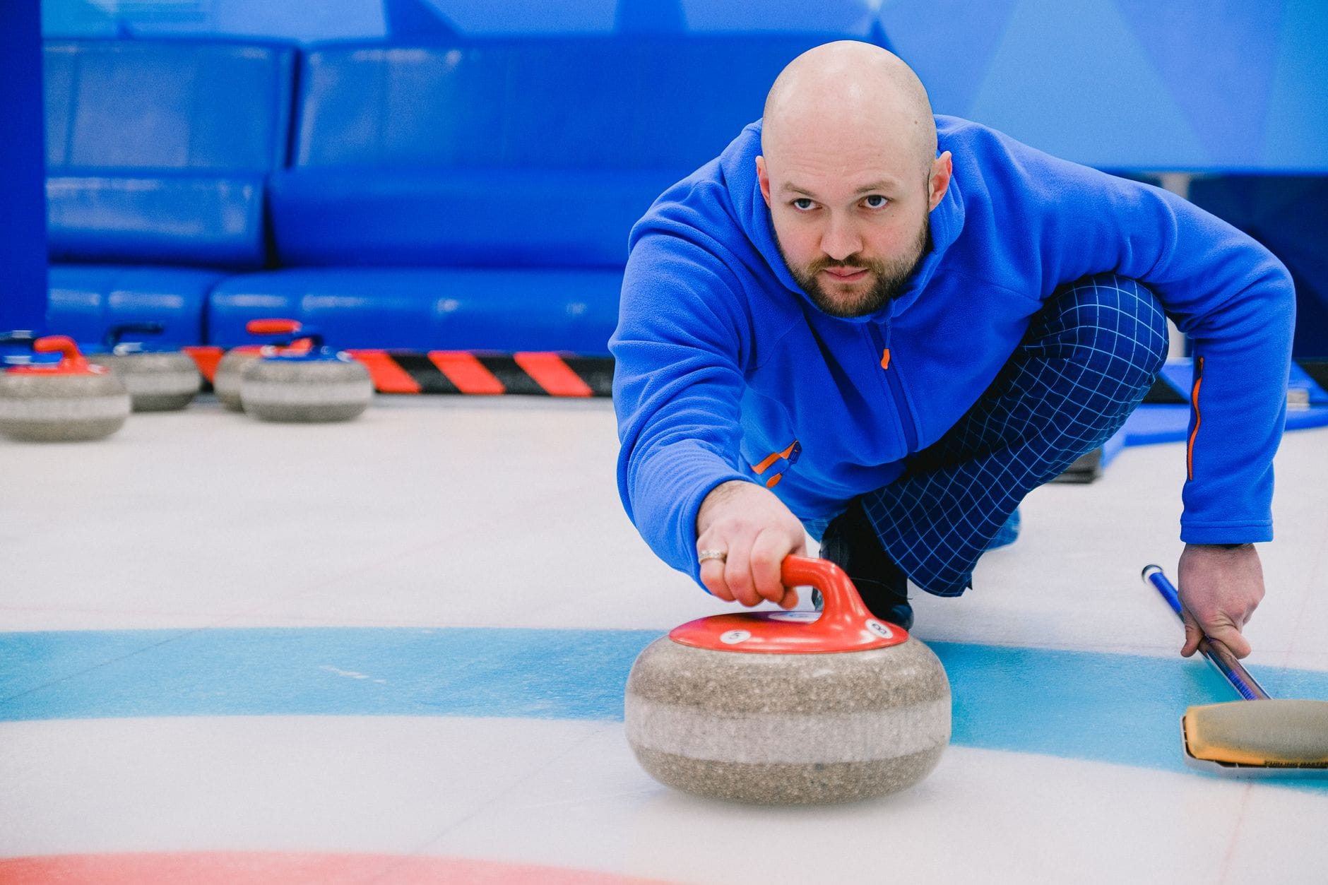 Zawodnik w niebieskim stroju wypuszcza kamień na lodowisku do curlingu
