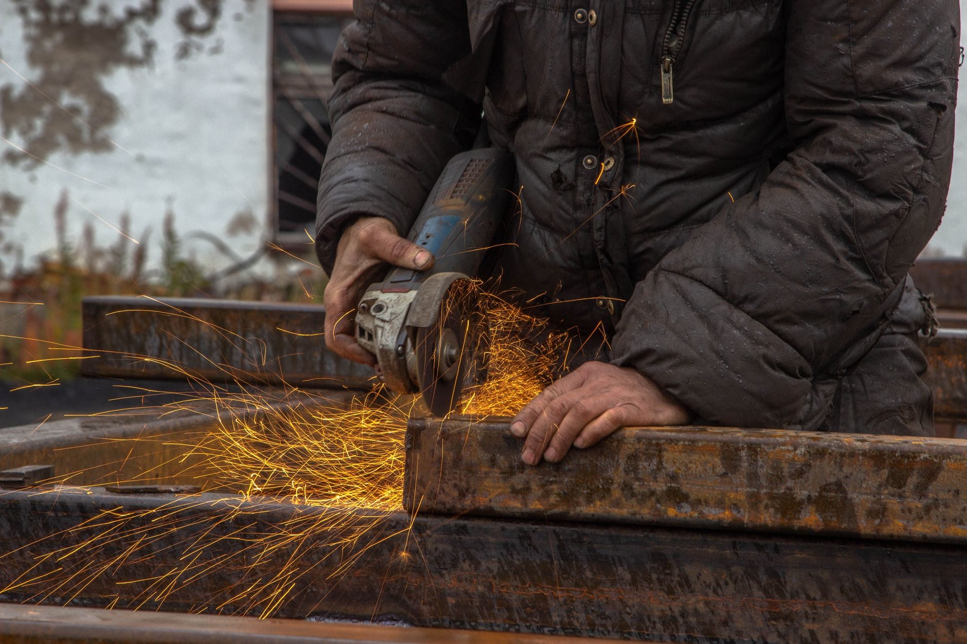 Pracownik szlifuje metal szlifierką kątową, lecą jasne iskry