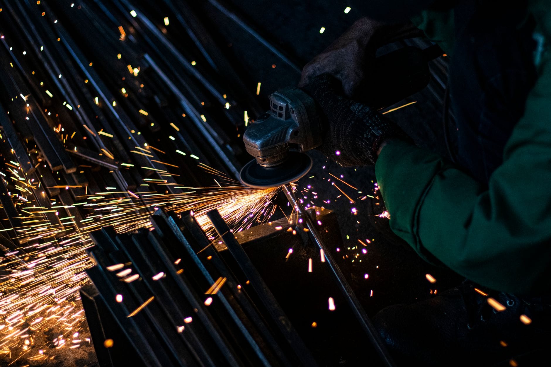 Pracownik szlifuje metal w ciemnym garażu, lecą jasne iskry
